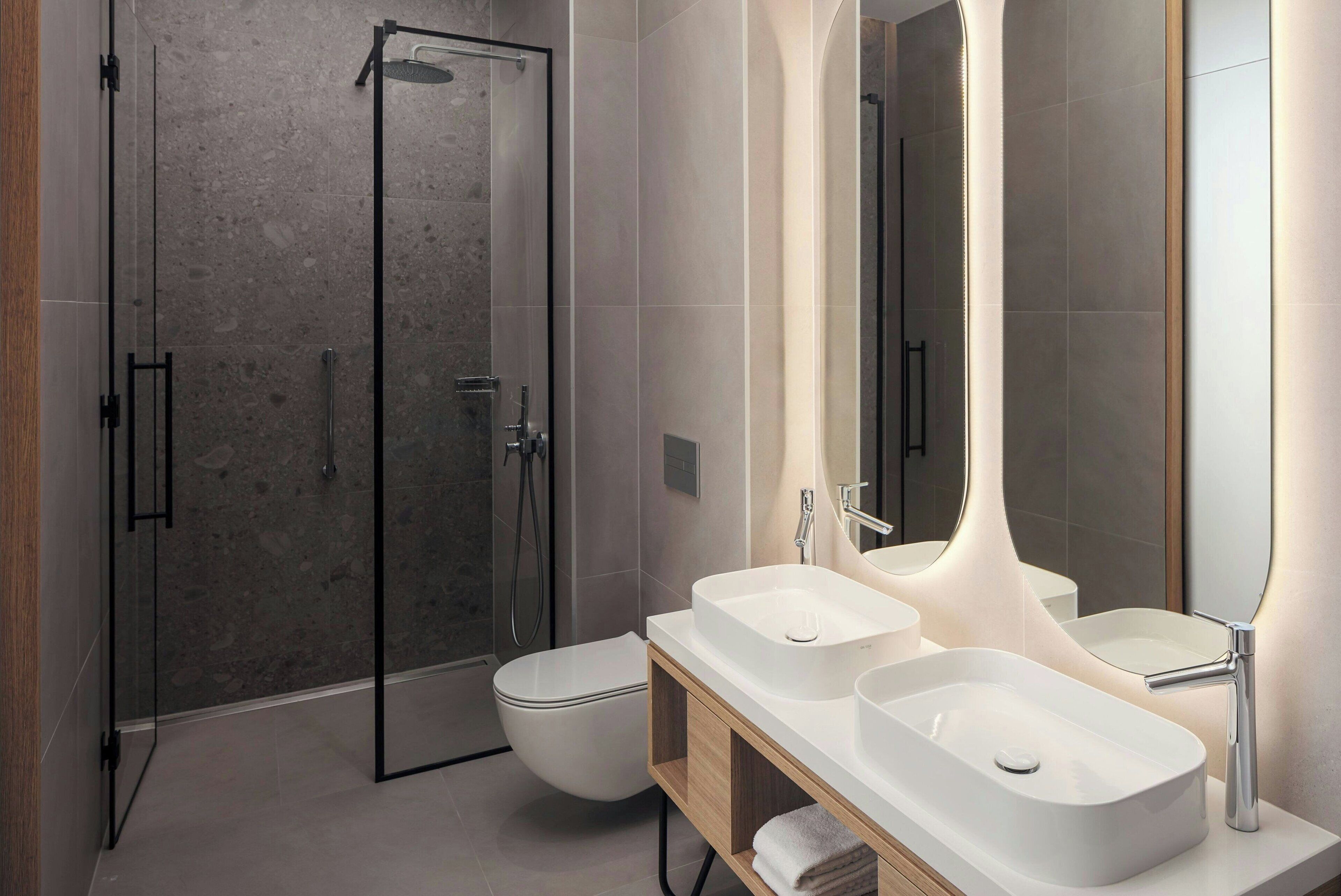 A modern bathroom with a glass-enclosed shower, a white toilet, and a vanity with two sinks and a mirror.