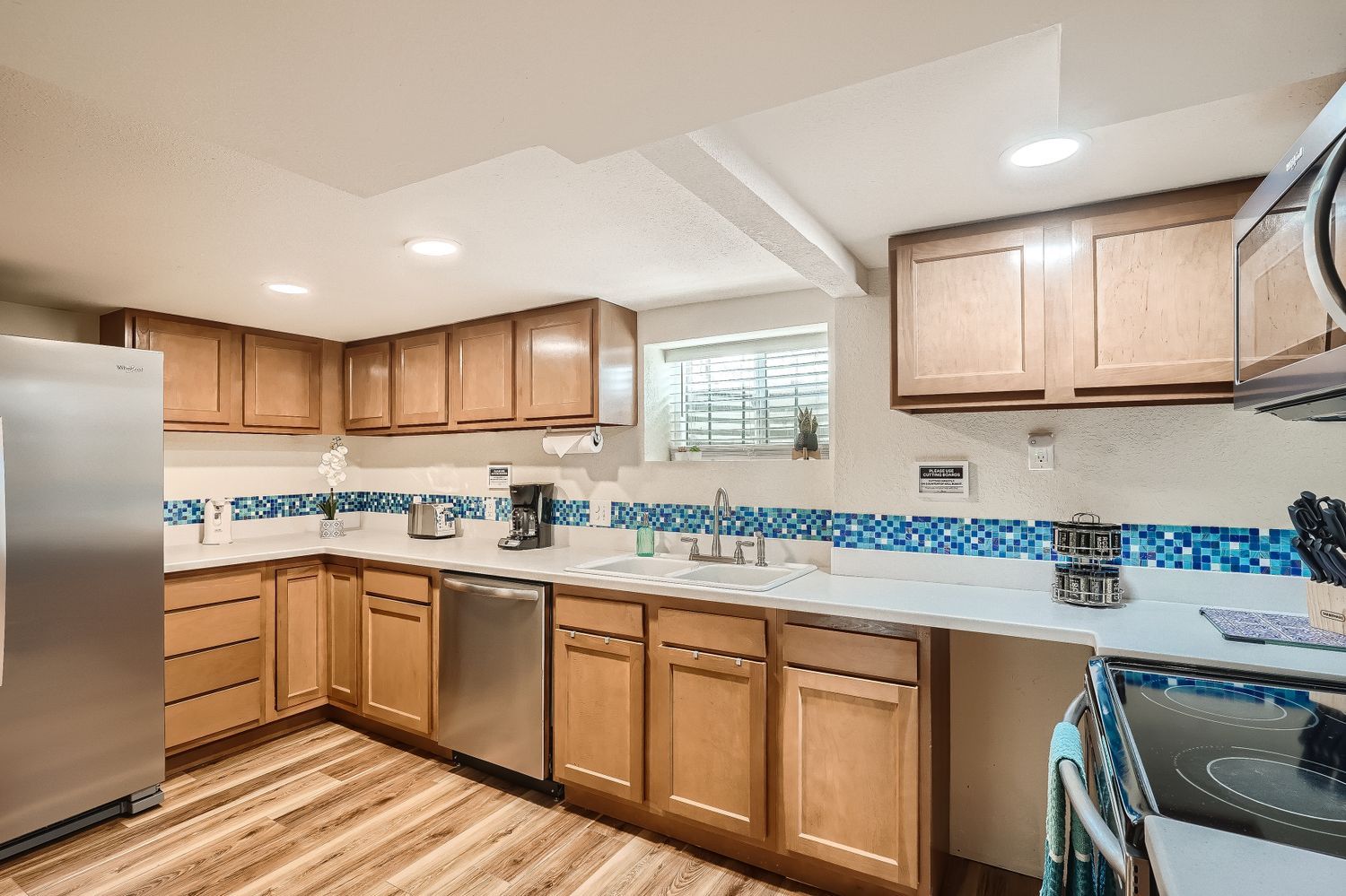 A modern kitchen with wooden cabinets, a stainless steel refrigerator, a dishwasher, and a tiled backsplash.