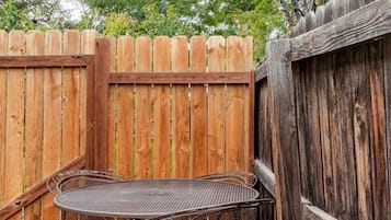 A metal table and chairs set up against a wooden fence in a garden area with gravel ground.