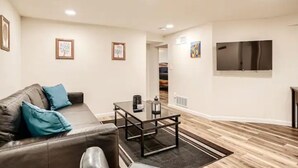 A modern living room with a leather sofa, a glass coffee table, and a flat-screen TV mounted on the wall. - Sloans Lake Getaway Near Broncos & Downtown Denver (Lakewood)