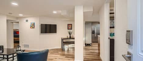 Una sala moderna con televisor de pantalla plana, comedor con mesa y sillas, y cocina con refrigerador y dispensador de agua.