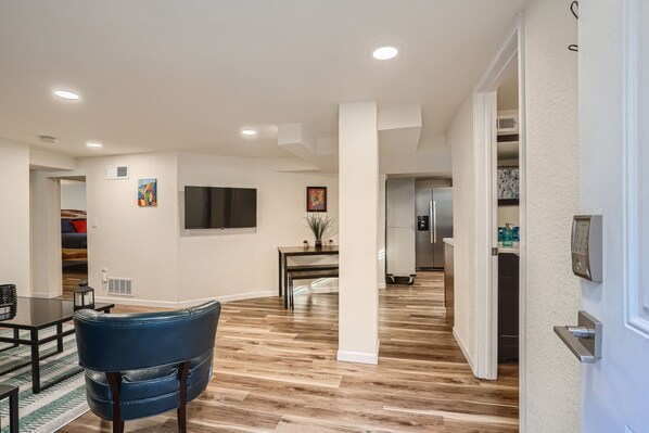 Una sala moderna con televisor de pantalla plana, comedor con mesa y sillas, y cocina con refrigerador y dispensador de agua.