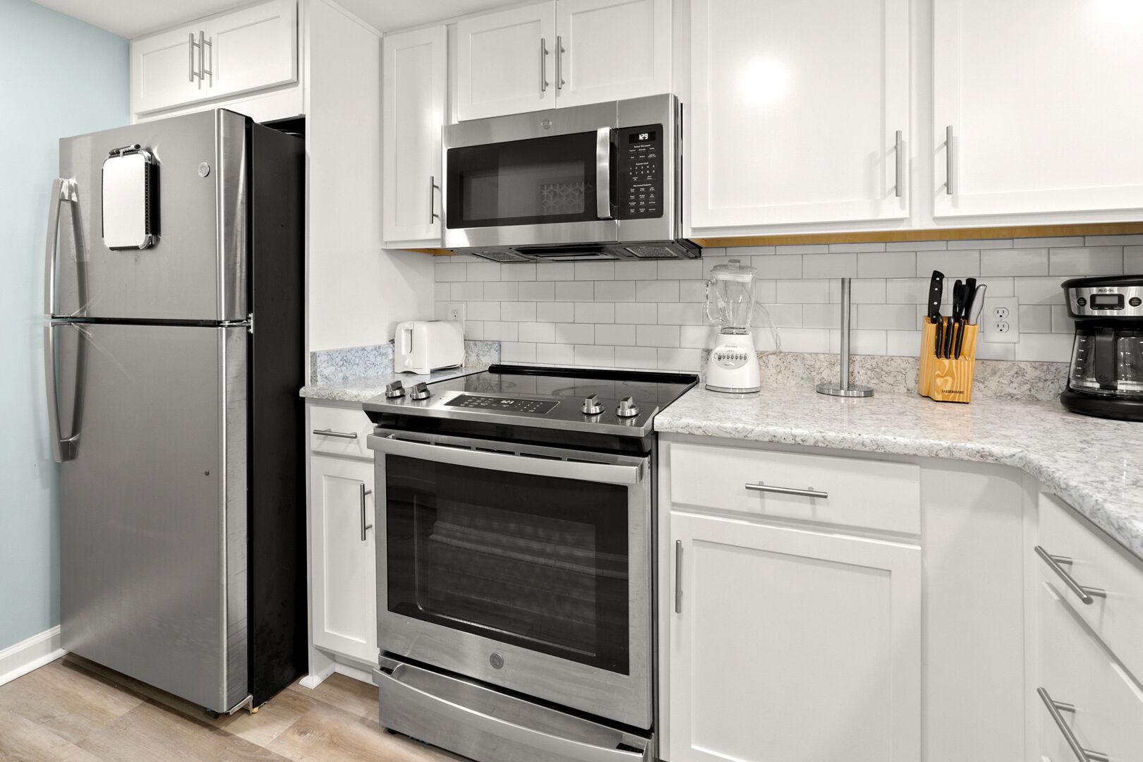 A kitchen with stainless steel appliances, white cabinetry, and a granite countertop.