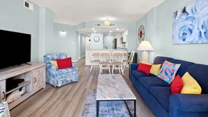 Un soggiorno moderno con televisione, un divano blu, una poltrona a fantasia e un'area pranzo sullo sfondo.
