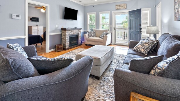 A living room with grey sofas, a fireplace, a ceiling fan, and a TV.