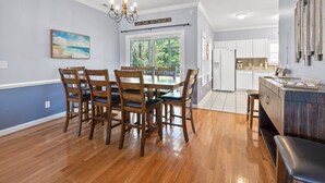 A dining area with a wooden table and chairs, a chandelier, and a view of the outdoors through a window.