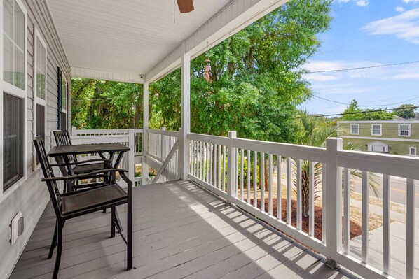 A covered porch with a table and chairs, white railings, and a view of a street and greenery. - Dog Friendly Luxe home/close to beach & Main Street-relaxing porches & yard (North Myrtle Beach)