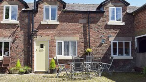 A two-story brick house with a front door labeled "GRANARY," a small garden with potted plants, and a metal table and chairs set up outside. - 3 bedroom accommodation in Burscough, near Southport (Burscough, near Southport)