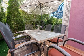 Een terras met een tafel en stoelen, omringd door groen en een roze muur.
