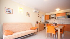 A compact living space with a sofa, dining table, and chairs, a kitchenette, and a wall-mounted air conditioner. - Modern flat with large terrace (Baska)