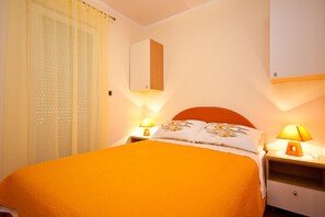 Hotelkamer met een bed, twee nachtkastjes met lampen, een spiegel boven het bed en een raam met dunne gordijnen.