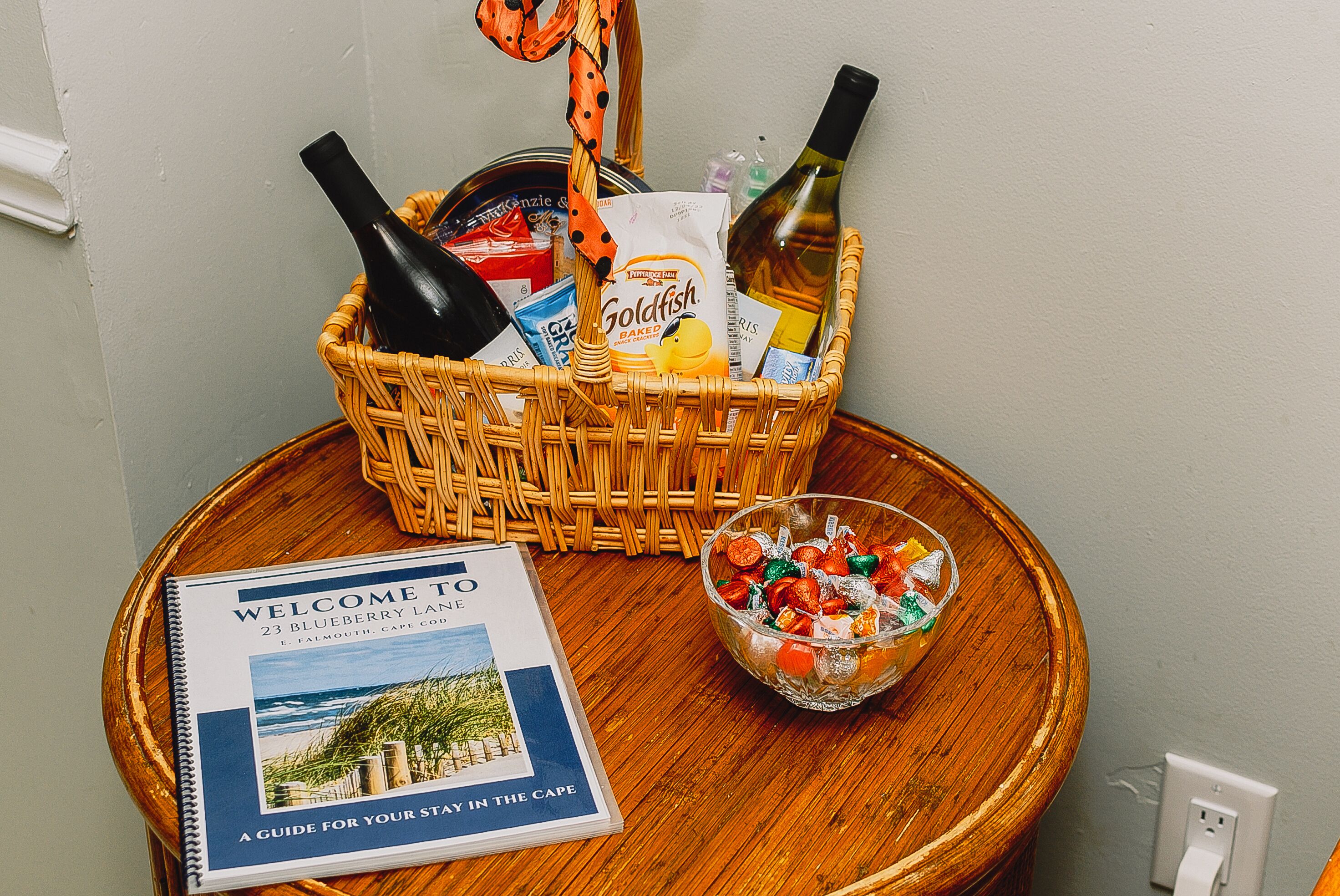 A wicker basket with bottles, snacks, and a brochure on a wooden table.