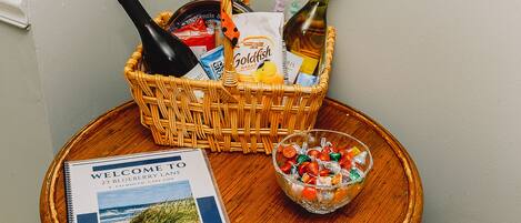 A wicker basket with bottles, snacks, and a brochure on a wooden table.