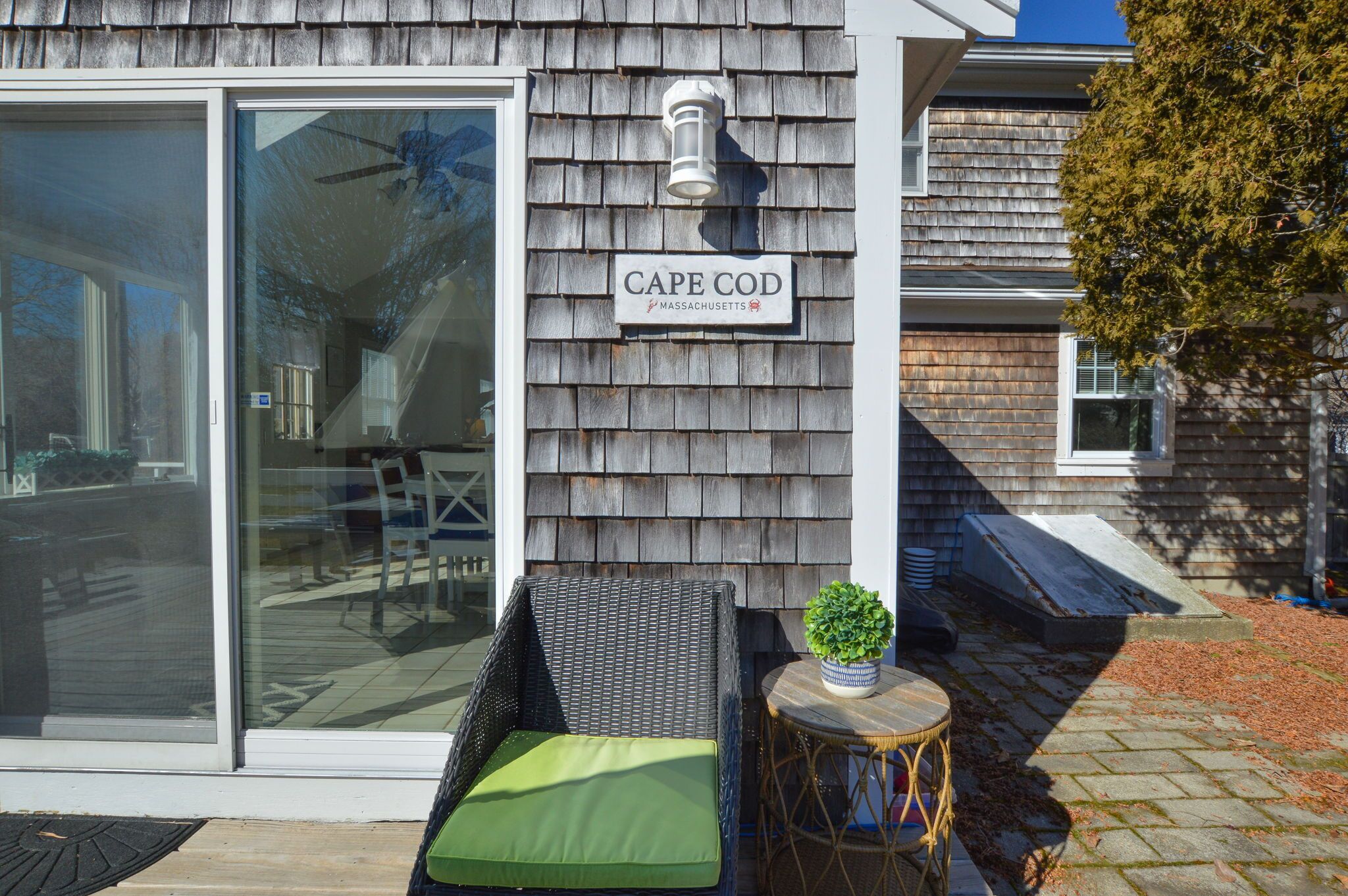 A house with a sliding glass door, a wicker chair with a green cushion, and a small round table with a potted plant.