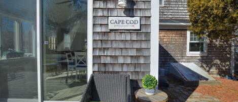 A house with a sliding glass door, a wicker chair with a green cushion, and a small round table with a potted plant.