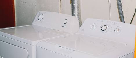 En bild som visar tvättmaskinen och torktumlaren framifrån. Båda är vita och har vred för inställningar samt en ventilationsslang.