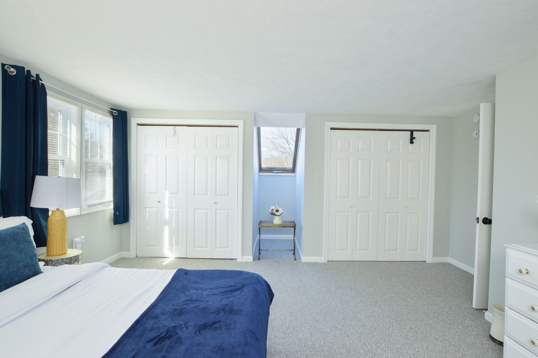 A bedroom with a bed, a nightstand, a lamp, a dresser, and two doors.