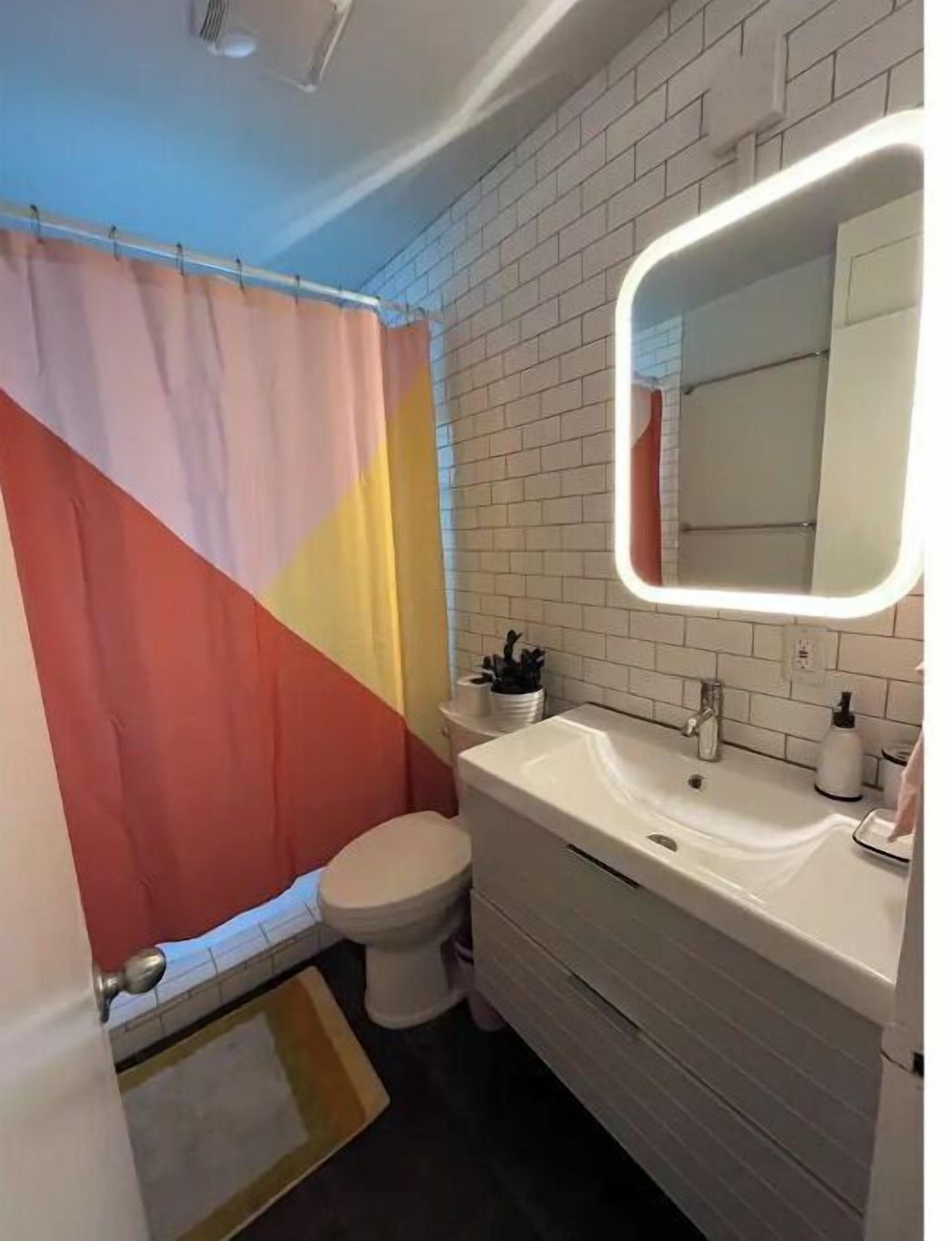 Un bagno con lavandino bianco, un water e una tenda da doccia a motivo geometrico.