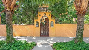 Una entrada con puerta, un arco decorativo, palmeras y un camino que lleva a un edificio.
