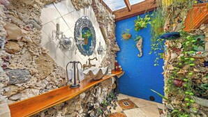 Baño con pared de piedra, pared azul y repisa de madera.