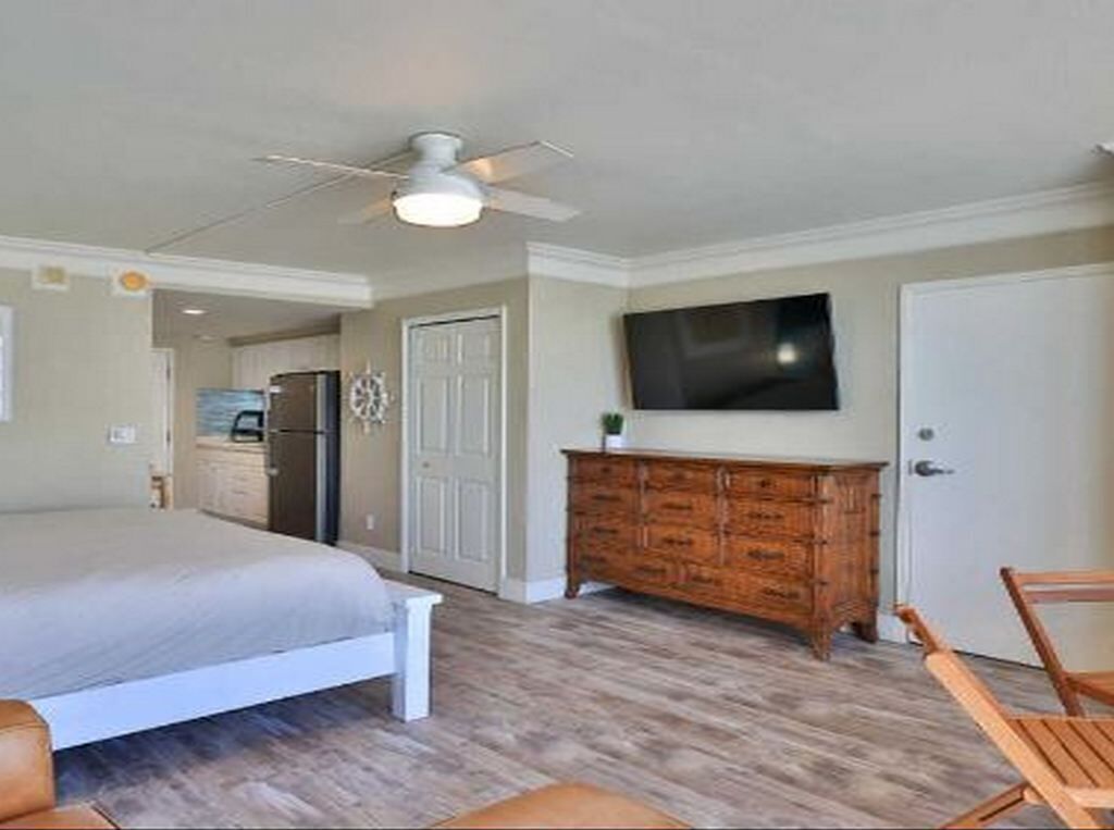 A bedroom with a bed, wooden dresser, TV, and a ceiling fan.