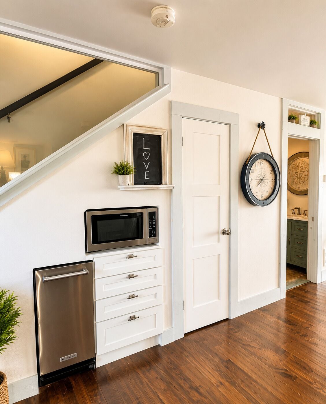 A kitchen with white cabinetry, a stainless steel refrigerator, a microwave, and a clock on the wall.