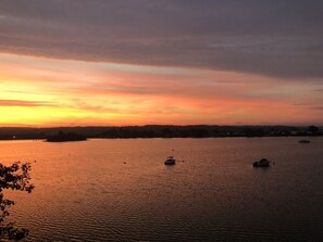 Un coucher de soleil sur une étendue d’eau calme, avec des bateaux.