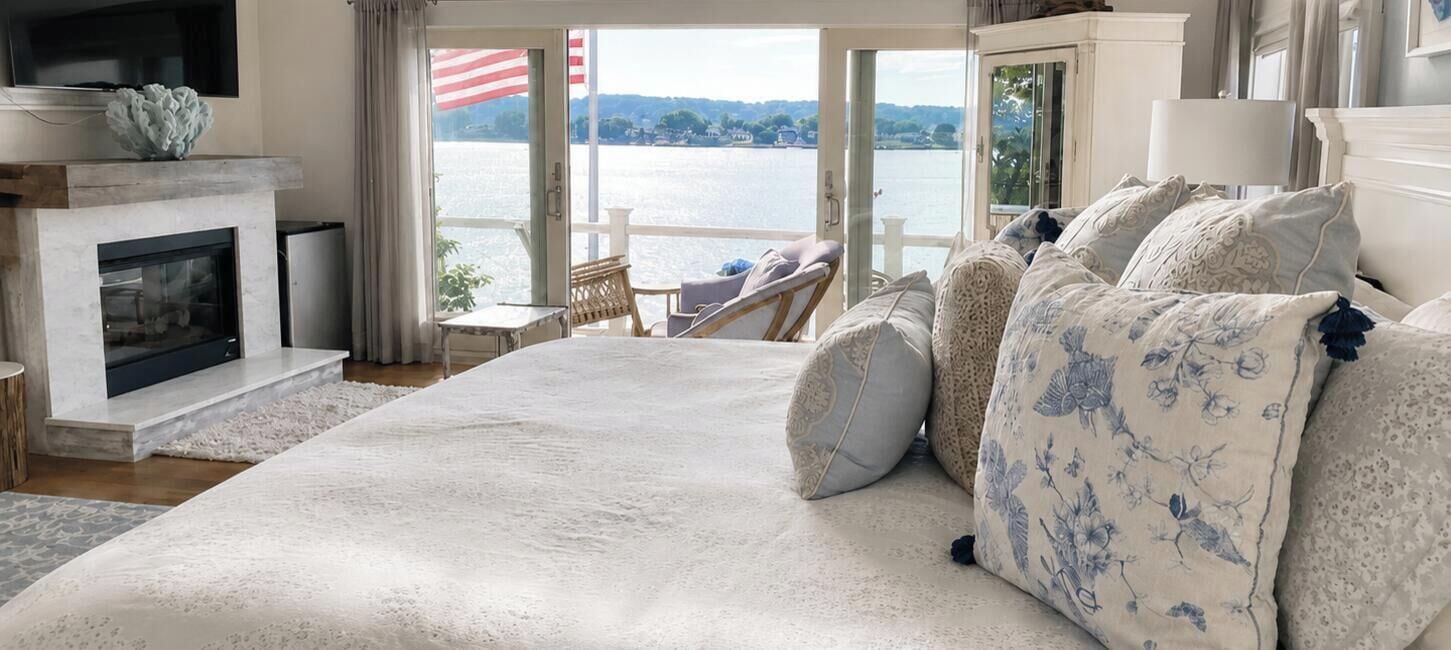 A bedroom with a large bed, a fireplace, a television, and a view of a lake.