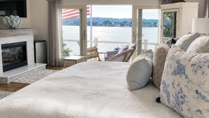 A bedroom with a large bed, a fireplace, a television, and a view of a lake. - Bella Vista, Luxury Waterfront Retreat Private Dock, Outdoor Living Near Newport (Portsmouth)