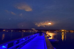 Une jetée en bois s’étendant sur une étendue d’eau calme, la nuit, avec un bateau amarré à son extrémité.