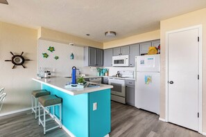 A modern kitchen with a central island, grey cabinets, a microwave, and a refrigerator.