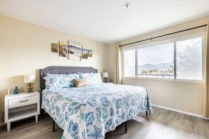 A bedroom with a bed, nightstands, a window with a view, and wall art.