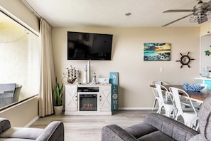 A living room with a fireplace, a television, and a dining area with white chairs.