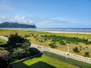 A coastal landscape with a paved walkway, grassy areas, and a view of the beach and ocean.
