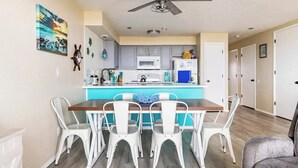 A modern kitchen with a central island, white chairs, and a ceiling fan. - Sand Dollar Haven at Seaside Beach Club Unit 306 (Seaside)