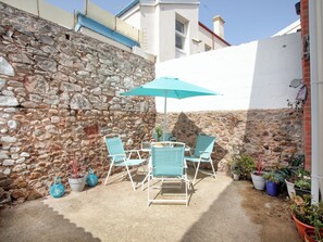 Un mur de pierre, un bâtiment blanc et un parasol bleu dans une cour.