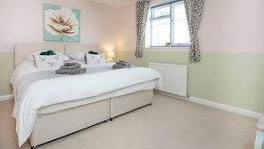 A bedroom with a large bed, a bedside lamp, a window with patterned curtains, and a wall-mounted artwork of a flower. - 2 bedroom accommodation in Dawlish (Dawlish)