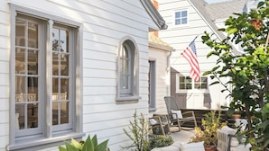 A white house with a porch, a white fence, and a small garden with plants and a sofa. - Classic Balboa Cottage, Newly Updated with A/C! (Newport Beach)