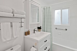 A modern bathroom with a white sink, mirror, and towel rack. There is a window with a frosted glass panel and a shower curtain.