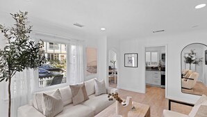 A modern living room with a white sofa, a coffee table, and a dining area with a kitchen in the background. - Classic Balboa Cottage, Newly Updated with A/C! (Newport Beach)