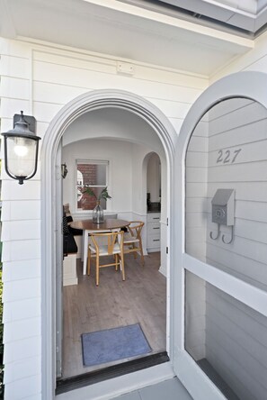 A modern kitchen with white cabinetry, a dining area with wooden chairs, and a mailbox with the number 227.
