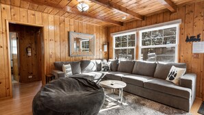A cozy living room with wooden walls and ceiling, a grey sectional sofa, a round coffee table, and a large bean bag.