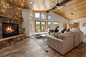 Un salón espacioso con chimenea de piedra, ventanas amplias y un techo alto.