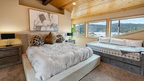 Une chambre avec un grand lit, un plus petit lit, un plafond en bois et une vue sur l’extérieur.