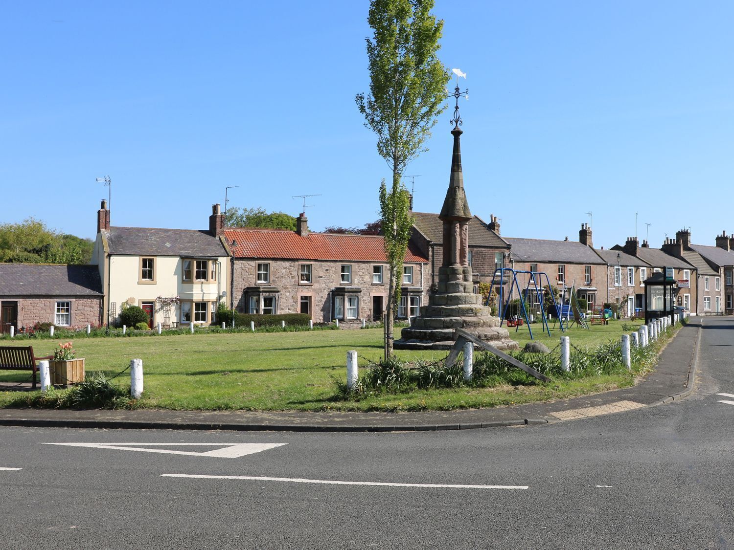 A residential street with houses, a central monument, and a playground.
