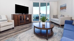 Ein Wohnzimmer mit Fernseher, einem Holzschrank, einem runden Couchtisch mit Pflanze, einem beigen Sofa und einem blauen Sofa.