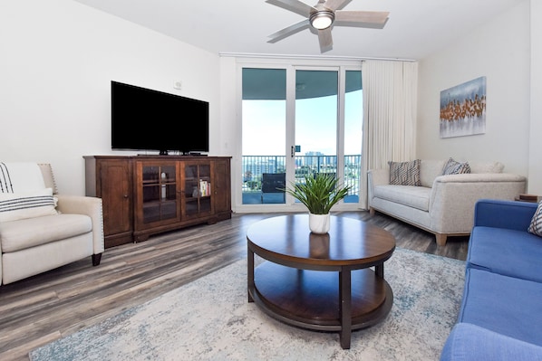 A living room with a flat-screen TV, a wooden cabinet, a round coffee table with a plant, a beige sofa, and a blue sofa. - Modern Condo on the 10th Floor of The Palms of Destin (Destin)