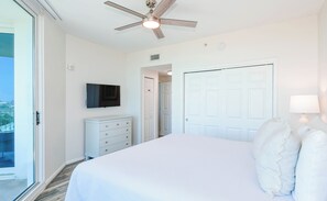 A bedroom with a bed, a TV, a ceiling fan, a dresser, and a door. - Modern Condo on the 10th Floor of The Palms of Destin (Destin)