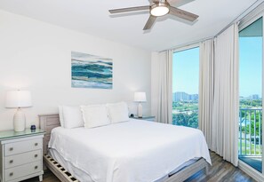 A hotel room with a bed, nightstands, a ceiling fan, a painting, and a large window with a city view. - Modern Condo on the 10th Floor of The Palms of Destin (Destin)