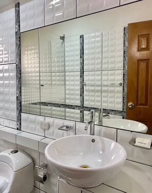 Un baño con un lavamanos blanco, un espejo grande y una puerta de madera.